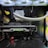 Inside view of a computer case showcasing a sophisticated gaming setup. Visible components include a GeForce RTX graphics card illuminated with green lighting, an ASUS motherboard, cooling fans with LED lighting, and a liquid cooling system with white tubes. Cables are neatly organized, and overall, the hardware suggests a high-performance machine.